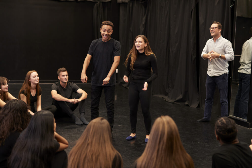 Teacher With Male And Female Drama Students At Performing Arts School In Studio Improvisation Class