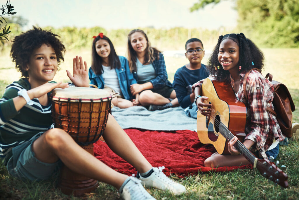 Shot of a group of teenagers playing musical instruments in nature at summer camp