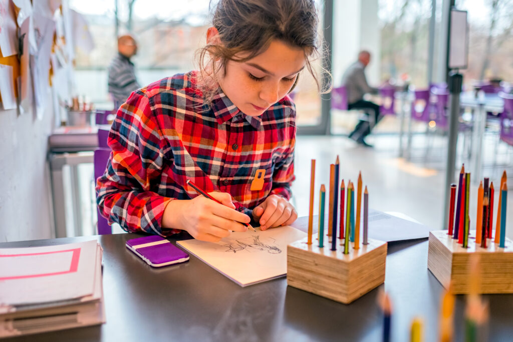 Cute schoolgirl drawing with pencils.